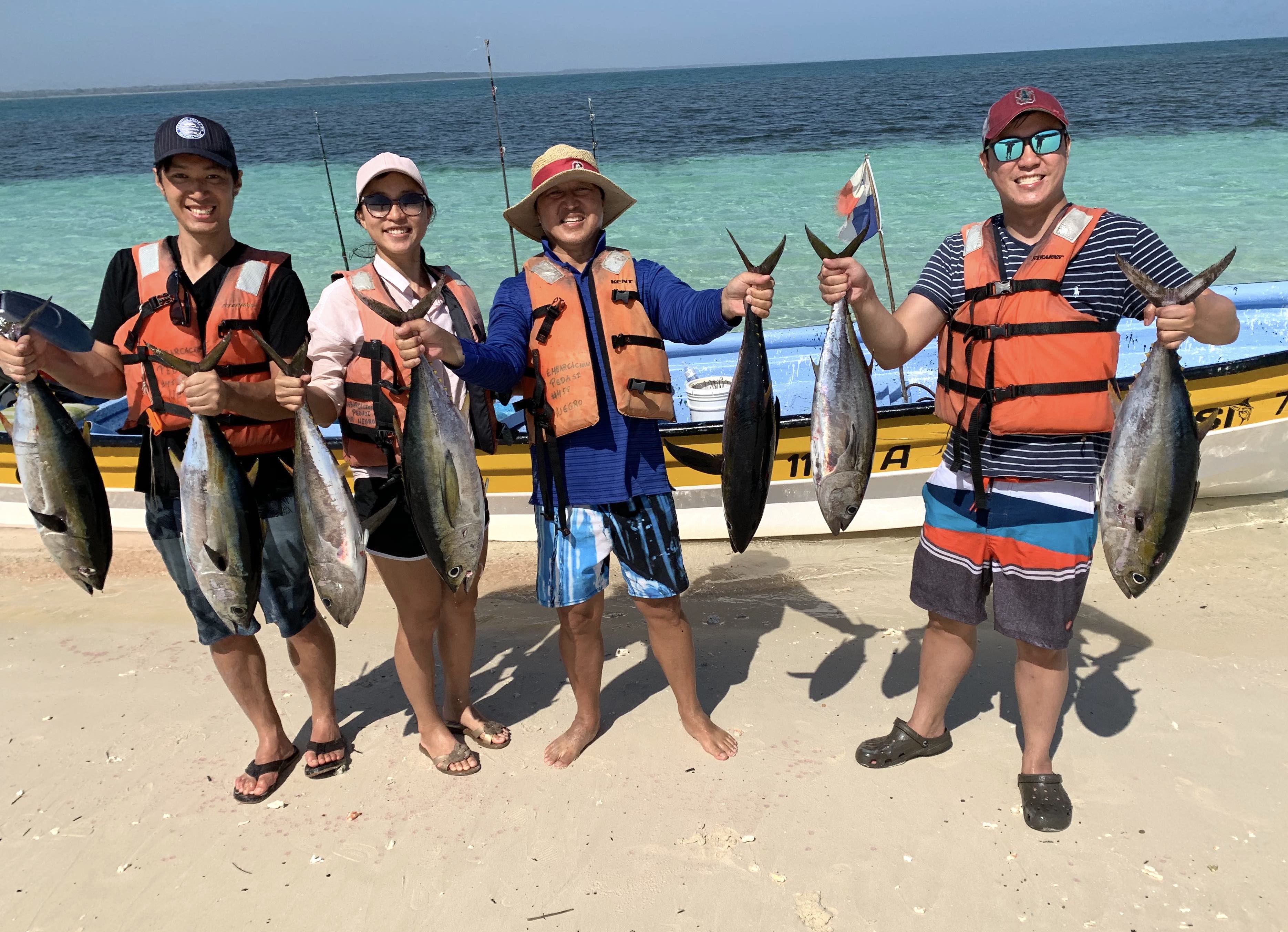 Four people holding yellowtail tuna standing in front of a fishing boat