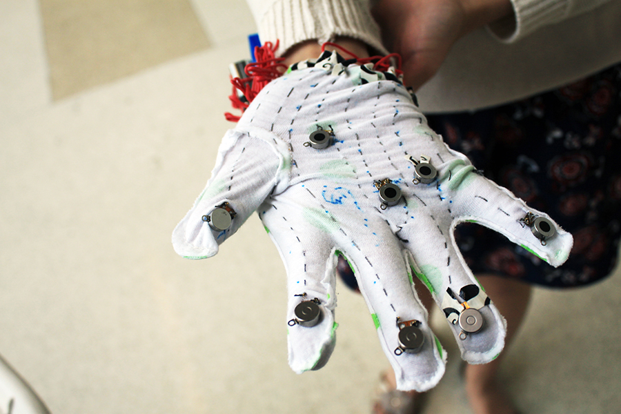 TouchMusic glove topview on a user's hand shows a white glove with flat coin cell vibration motors sewed around the glove with gray conductive thread.