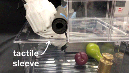 A robot arm with a custom designed 2-DOF wrist that wears a white sleeve with soft pneumatic sensors. The robot is reaching into a fridge drawer to retrieve a pear.
