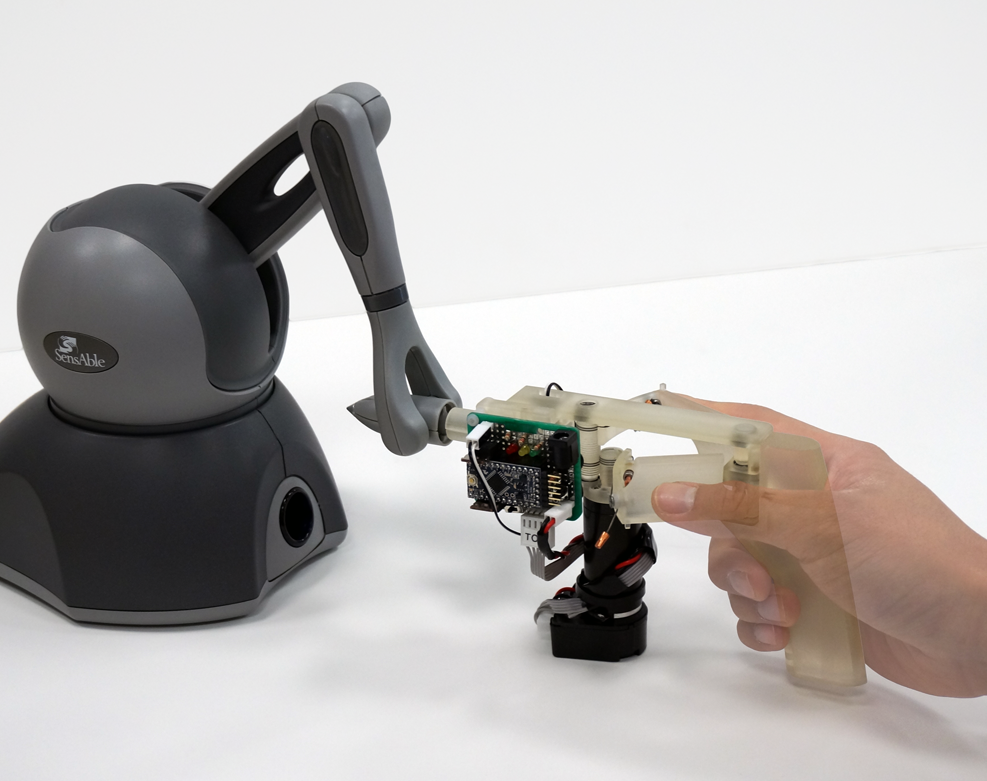 Photo of a haptic device attached to a Phantom Omni haptic manipulator and a user holding the device.
